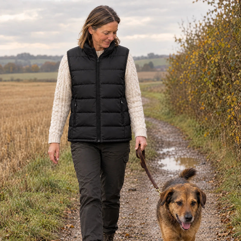 Woman walking her dog on a farm track in autumn, wearing the heated vest over a knit sweater